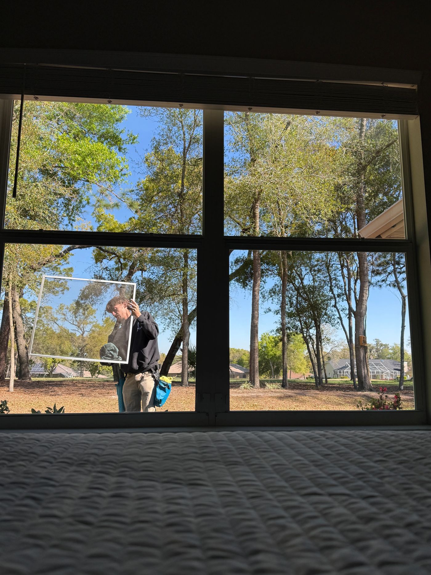 View from inside a home through a spotless picture window while a Brotherz technician removes the screen outside