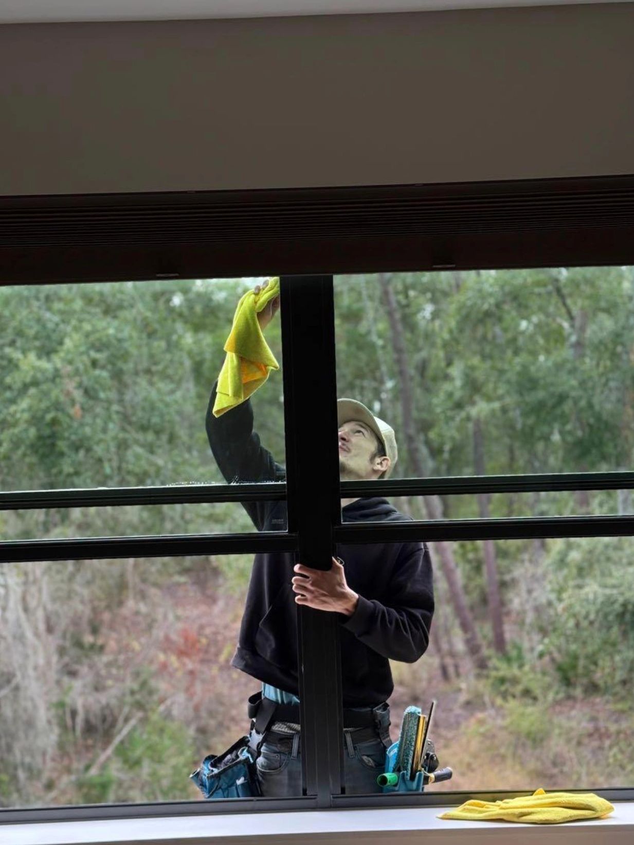 Brotherz technician hand-detailing the top edge of a tall window with a microfiber cloth