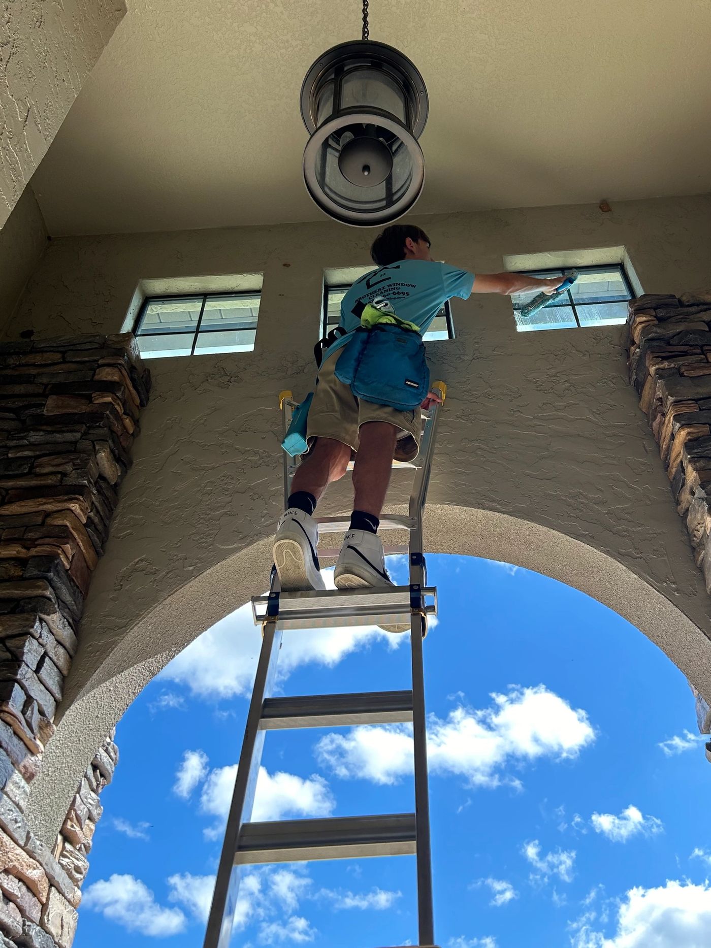 Brotherz technician on a ladder cleaning high transom windows above an arched entryway
