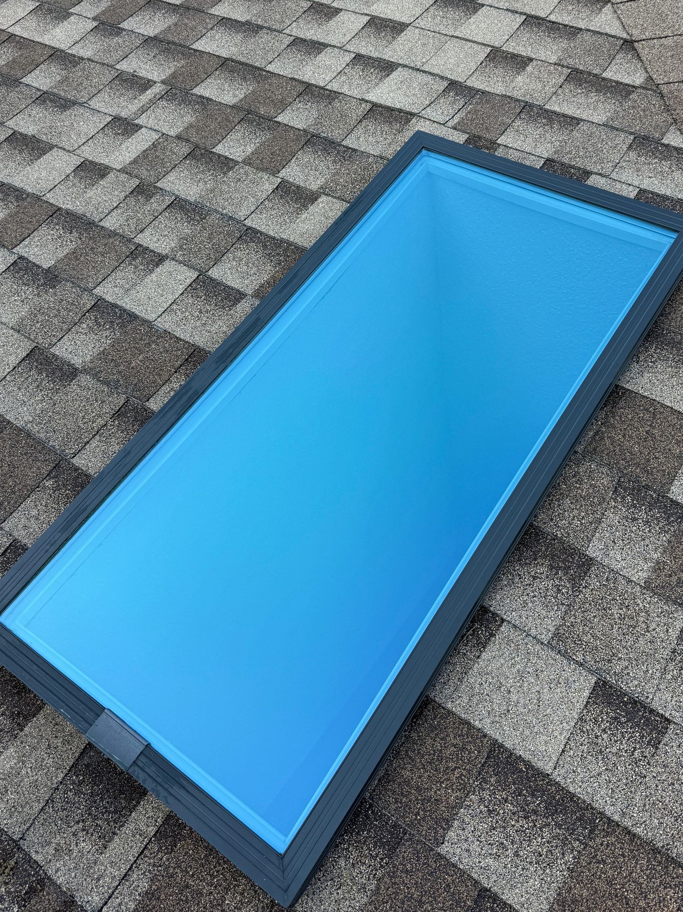 Spotless skylight on a shingle roof reflecting clear blue sky